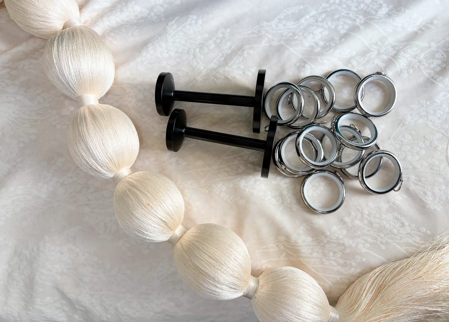 Steel curtain rings, black wall holdbacks and silk tassel trim laid out on a fine patterned white sheer.