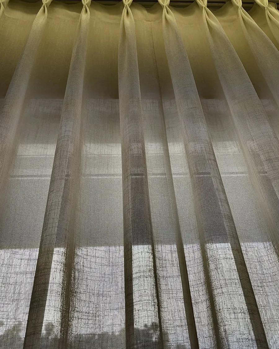 The pinch-pleat heading of a sheer, seen from below against the light.